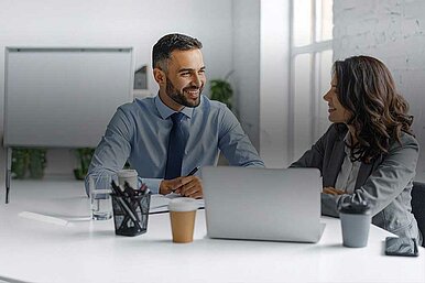 Zwei Geschäftspersonen beim Business-Meeting im modernen Büro mit Laptop, Kaffeetassen, Whiteboard und Regal