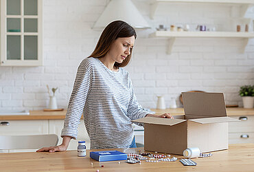 Frau blickt zuhause verunsichert auf ihr Paket mit Medikamenten