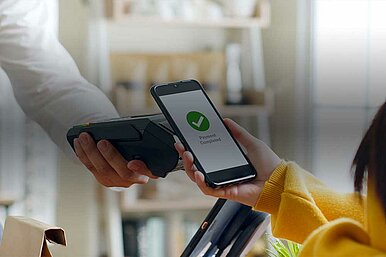 Nahaufnahme einer kontaktlosen Smartphone-Zahlung an einem Kartenlesegerät mit Bestätigung ‚Payment Completed‘