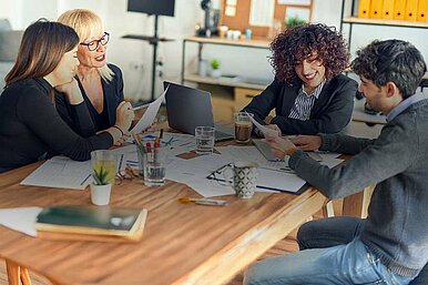 Vier Personen sitzen am Tisch und besprechen sich