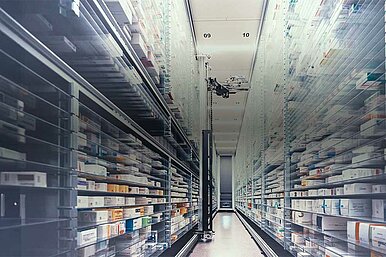 Automatisiertes Apothekenlager mit Regalen voller Medikamentenpackungen und einem Roboterarm zur effizienten Lagerverwaltung