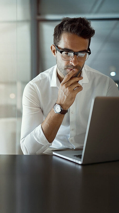 Geschäftsmann in weißem Hemd arbeitet konzentriert an einem Laptop in einem modernen Büro