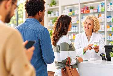 Eine Apothekerin berät eine Kundin, während zwei weitere Apothekenkunden in der Warteschlange warten