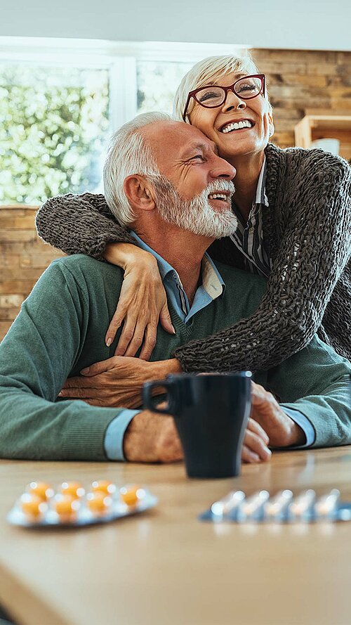 Glückliches älteres Paar lacht und umarmt sich liebevoll in moderner, sonniger Küche – Lebensfreude im Alter.