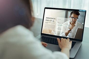 Person arbeitet im modernen Büro an Laptop mit geöffneter ADGCOACH PRO-FIT AI Login-Seite