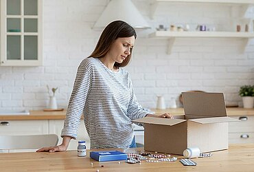 Frau blickt zuhause verunsichert auf ihr Paket mit Medikamenten