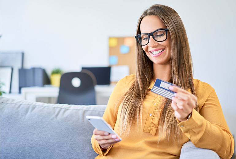 Frau sitzt auf Sofa und hält Smartphone und Krankenkassenkarte in der Hand