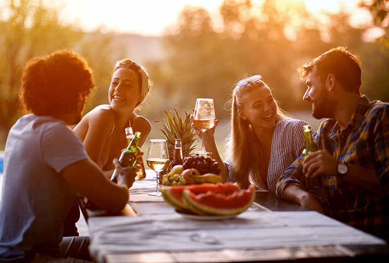Menschen machen ein Picknick und trinken Wein bei Sonnenuntergang
