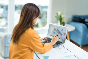 Frau in gelber Bluse analysiert bunte Balkendiagramme auf einem Laptop in einem modernen Büro