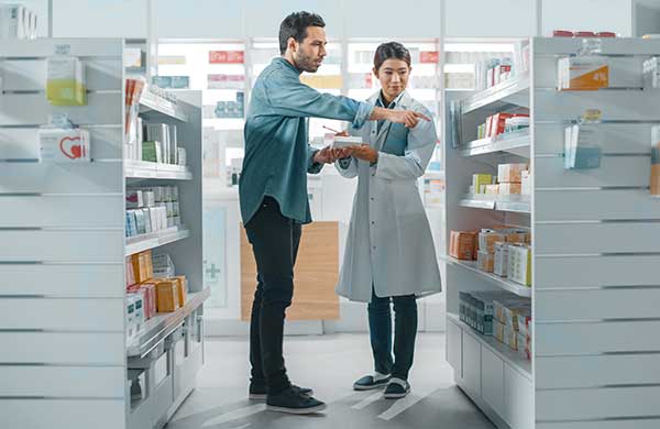 Mann steht neben Apothekerin und zeigt auf Regal