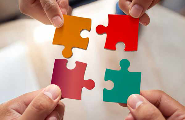 Vier Hände fügen farbige Puzzleteile zusammen – Symbolbild für Teamarbeit, Zusammenarbeit und gemeinschaftliche Lösungsfindung